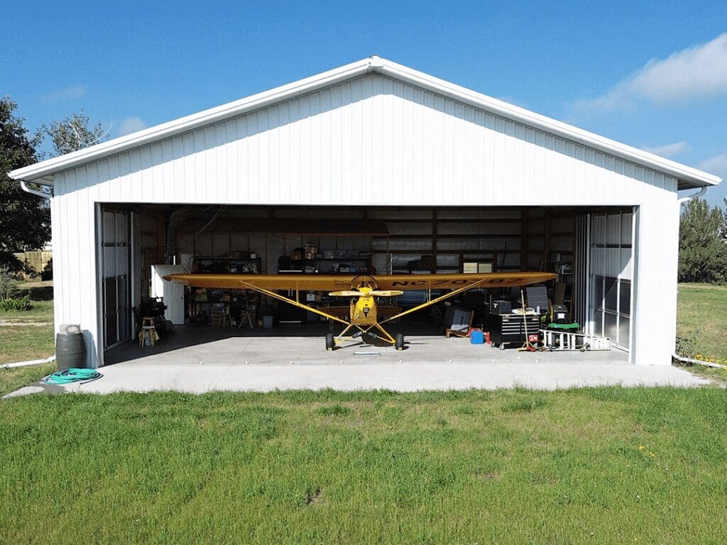 yellow airplane parked inside of a white stell structure pole hanger