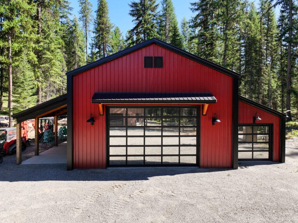 Red and black post-frame shop with lean-to built in a wooded setting
