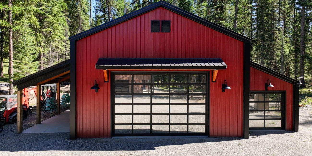Red and black post-frame shop with lean-to built in a wooded setting