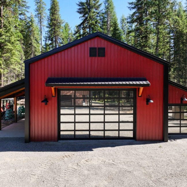 Red and black post-frame shop with lean-to built in a wooded setting