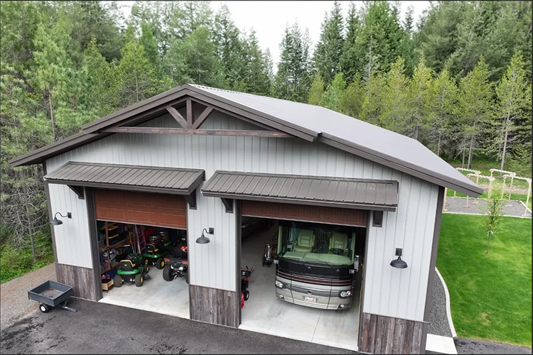 A metal building used as a shop has its large doors open to fit an RV and ATVs