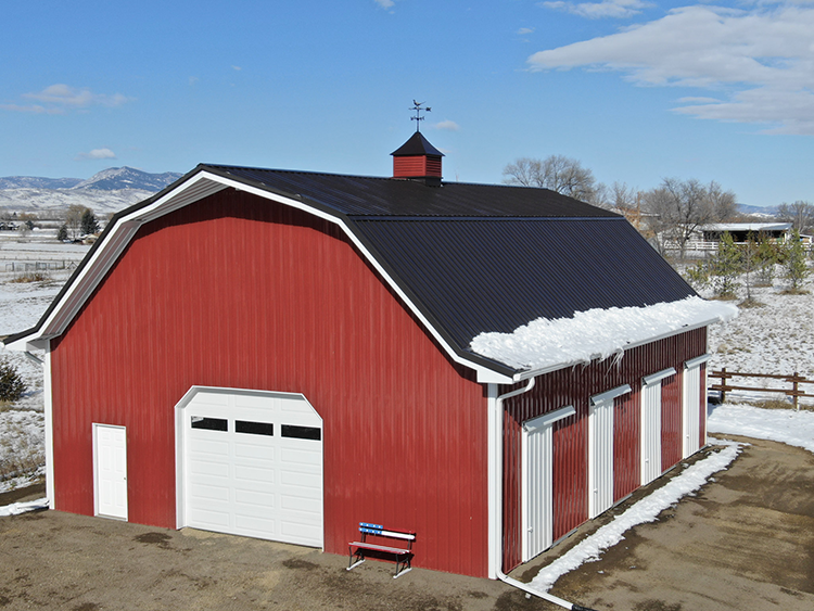A red gambrel pole barn with white trim, built by Steel Structures America
