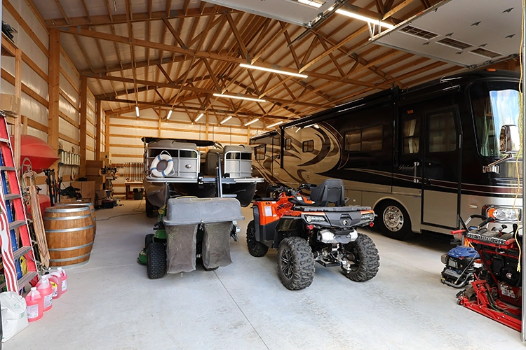 A large RV is pictured in a mid sized shop alongside a boat and some ATV's