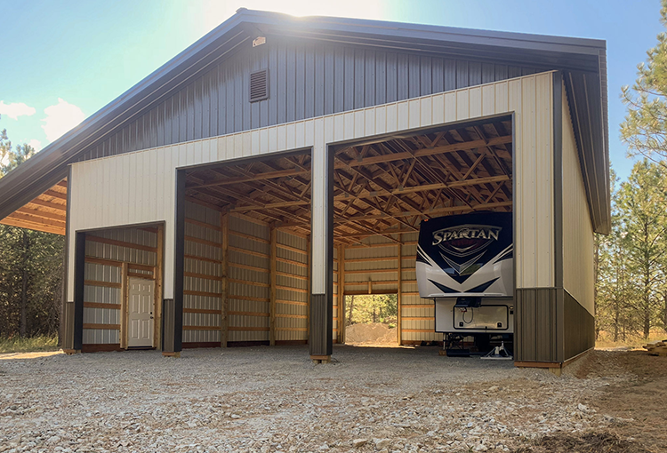 A pole barn shop has large overhead doors open with a trailer inside