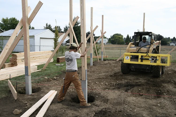 Workers install supports for a pole barn garage according to building code