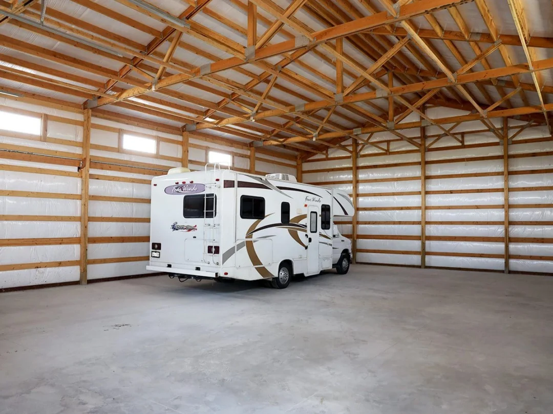 A small RV is parked in the corner of a large open pole-building shop