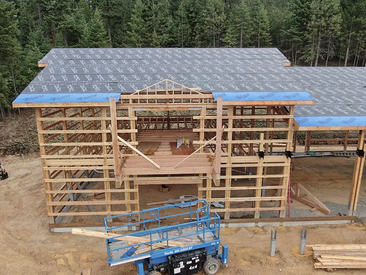 A pole barn construction site is prepped and heavy machinery is installing pieces of the pole barn