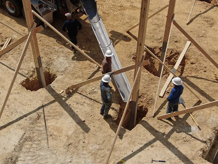 Workers pour concrete around a pole barn post in the ground