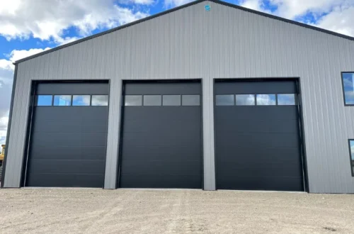 Commercial Flush Panel Garage Doors Three black flush panel commercial garage doors on a metal building