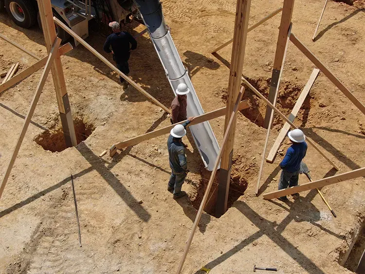 Workers pouring concrete around an in-ground post, the traditional way of setting poles for pole barn builds