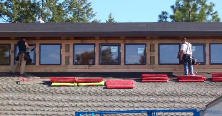 Two workers installing steel building windows into a framed post-frame wall