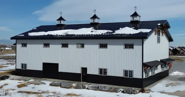A white two story pole barn with living quarters above the shop and a black metal roof