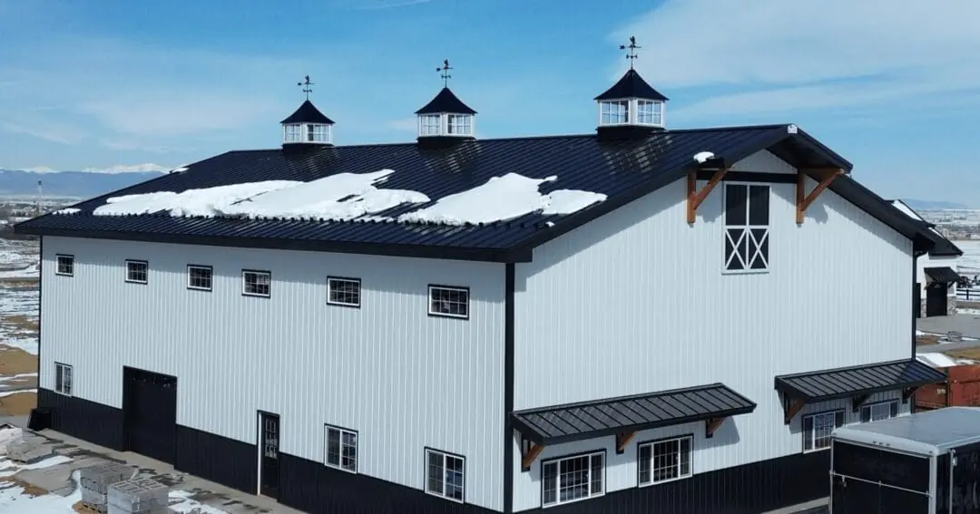 A barndominium that looks like a farmhouse, with a covered porch, gable accents, and a metal roof