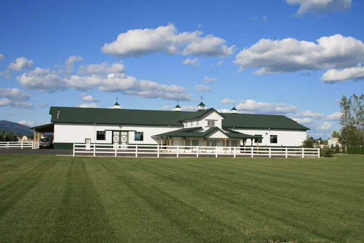 A white barndominium that looks like a farmhouse with black trim and a metal roof