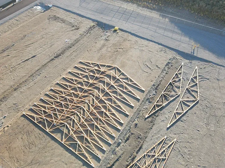 A post-frame roof truss leaning against stacked lumber, the engineered wood behind most metal pole barn trusses