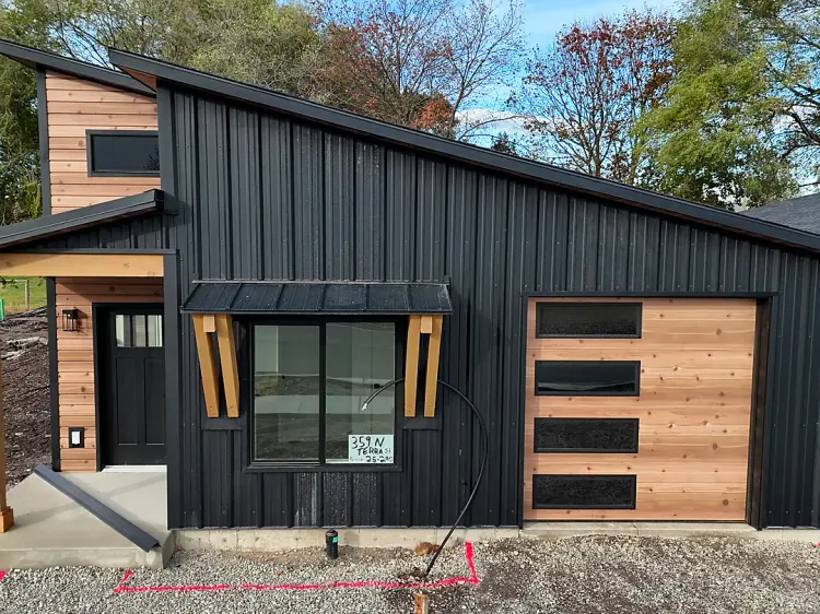 Pecky Cypress woodgrain metal siding accents on a black metal home, a warm pairing for a black metal building